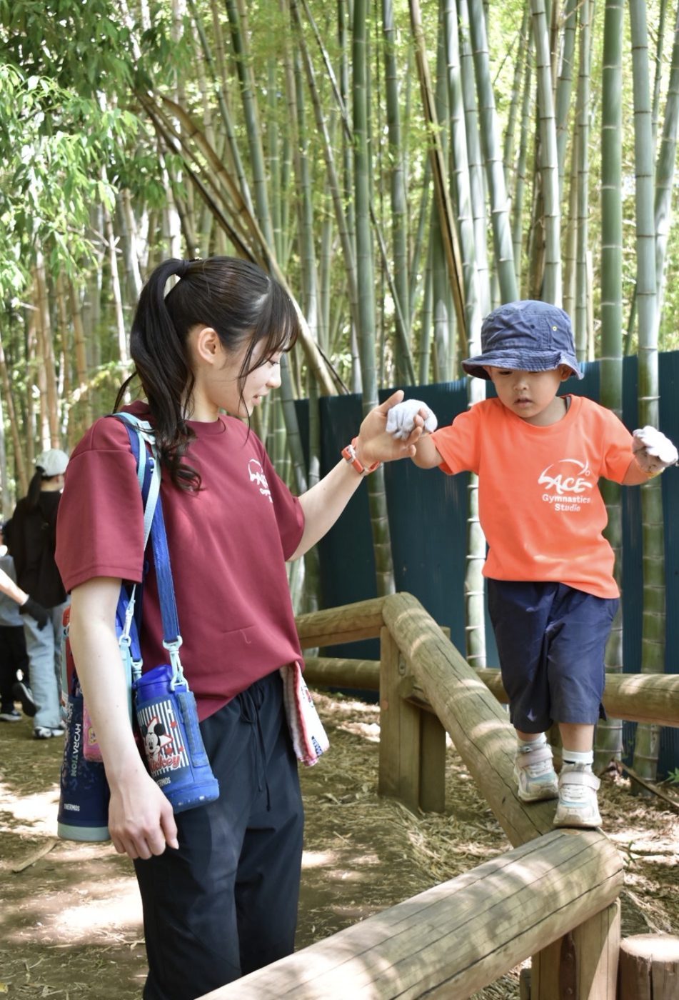 先生と手をつないで丸太を渡る子ども