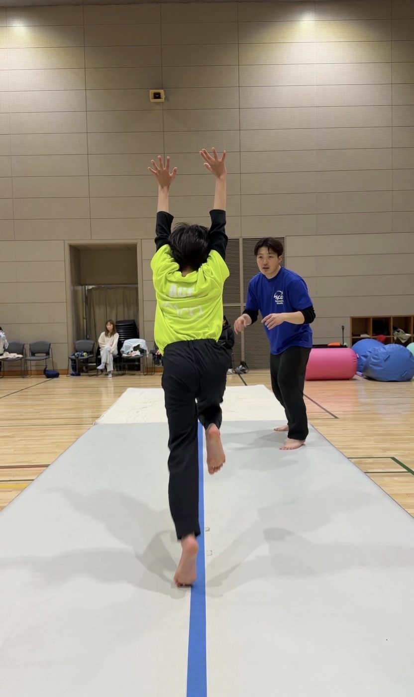 エアトラックで跳ぶ男の子と見守る先生